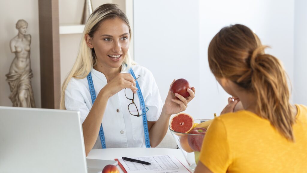 Na zdjęciu dietetyczka tłumaczy drugiej kobiecie, jaka dieta przy wysokim cholesterolu będzie najlepsza.