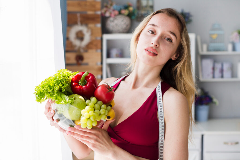 Jak schudnąć 3 kg? Dietą i ćwiczeniami! Na zdjęciu młoda kobieta trzymająca w dłoniach warzywa i owoce.