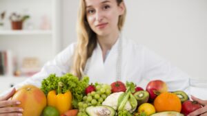 Na zdjęciu przestrzeganie diety omawiane przez dietetyczkę. Przed nią zdrowe produkty spożywcze.